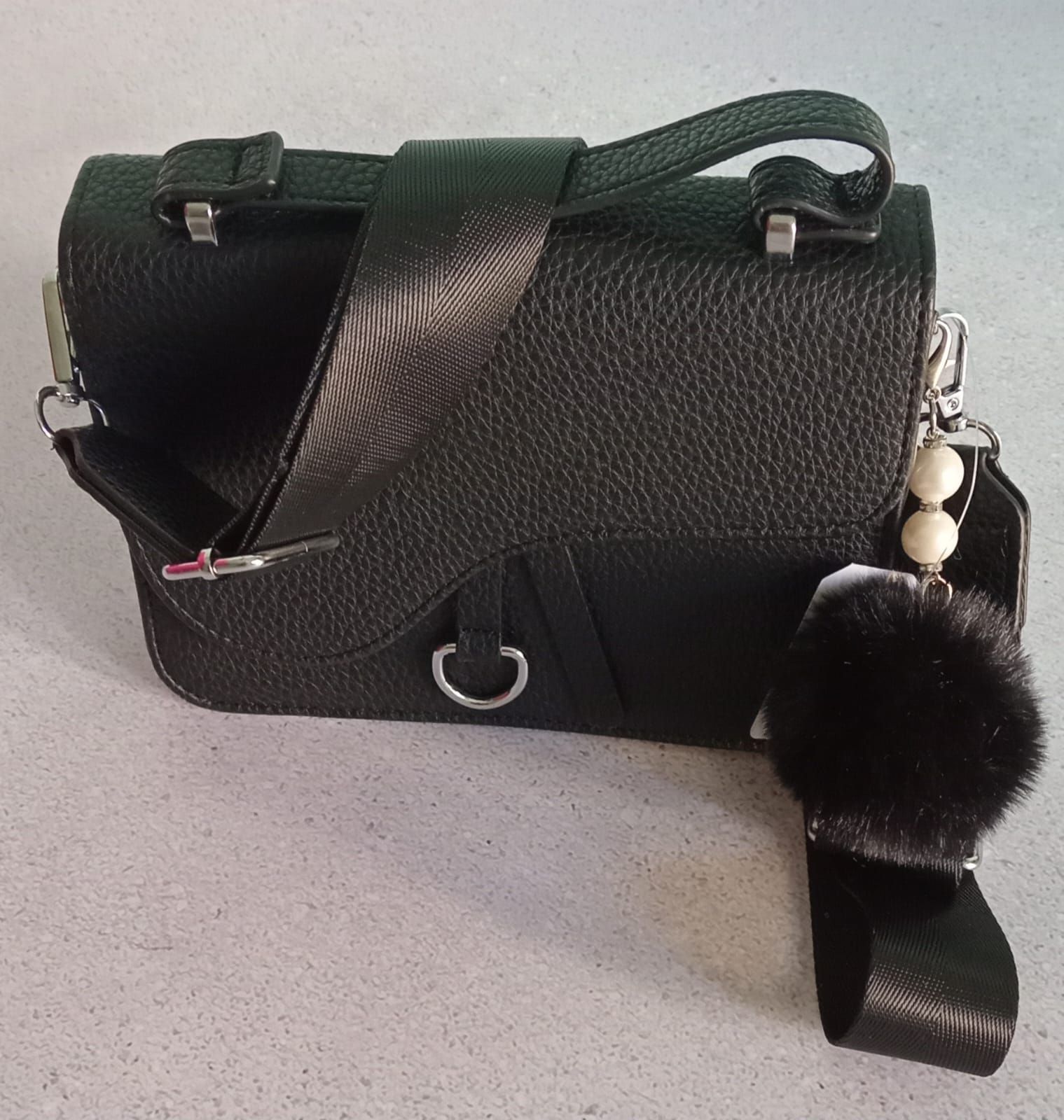 Dos bolsos con forma de silla de montar, en color tostado y negro, con correas para los hombros y adornos de pompones.