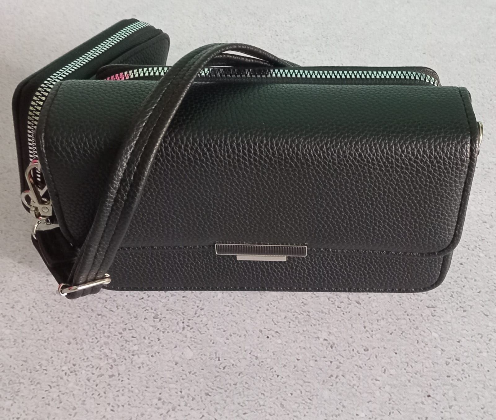 Bolso de mano negro con cartera a juego sobre superficie clara.