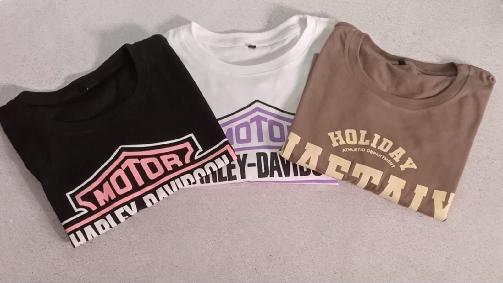 Tres camisetas: negra, blanca y marrón. Cada una tiene un logotipo. La camiseta negra dice 