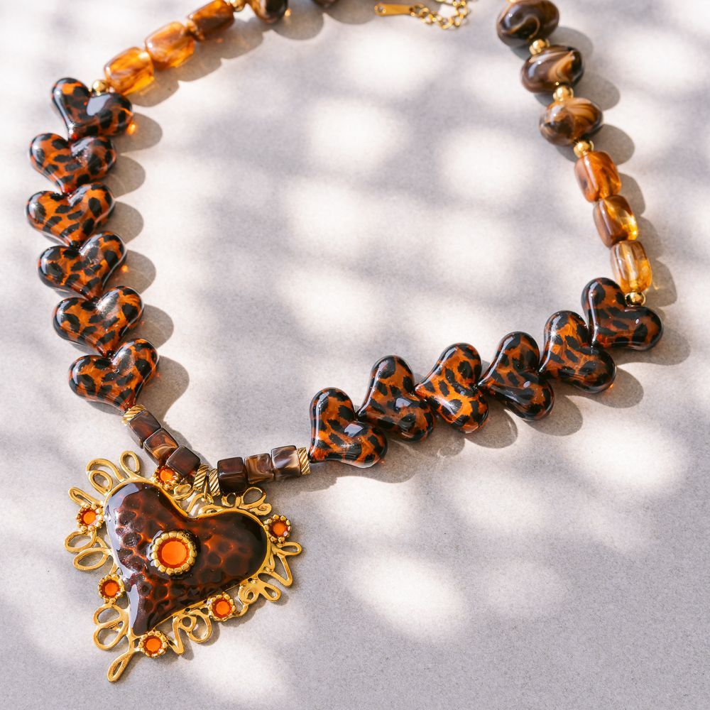 Collar de cuentas ámbar y negras con un colgante en forma de corazón sobre un fondo estampado claro.