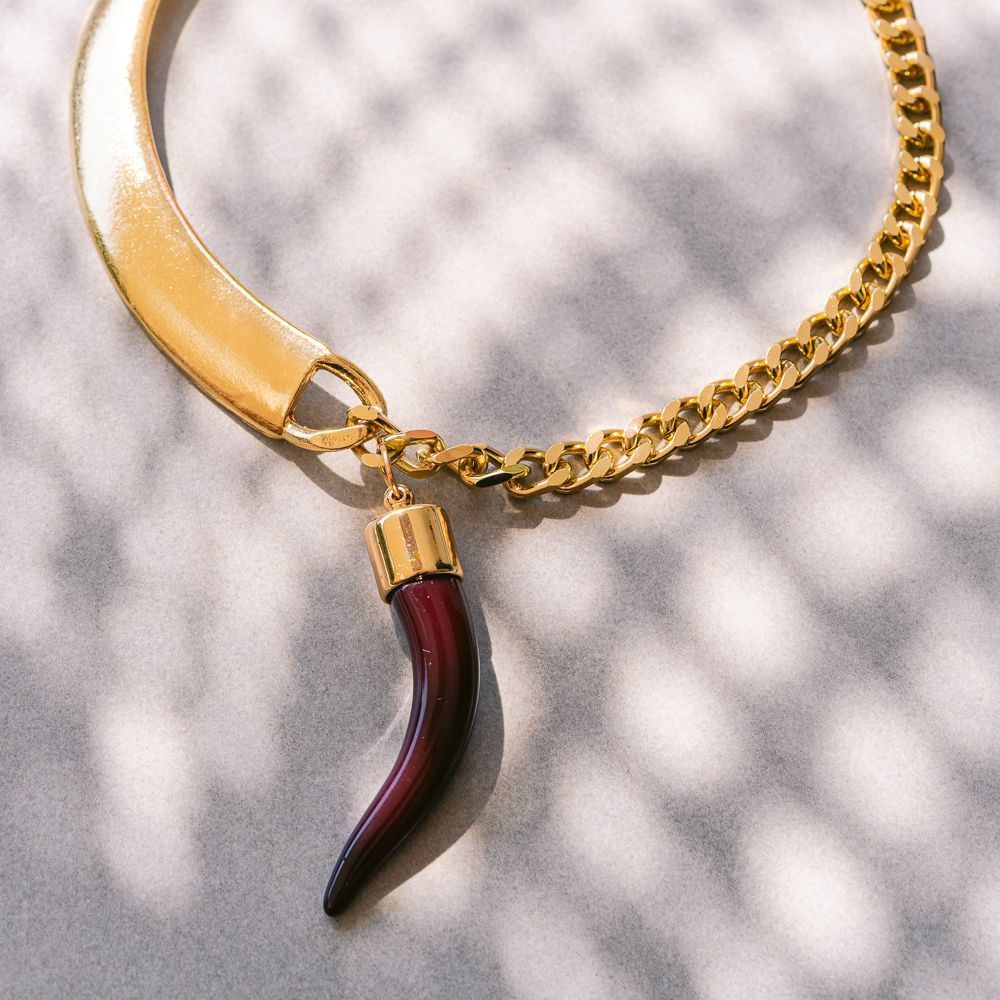 Collar de oro con un colgante de cuerno rojo sobre un fondo de tela estampada clara.