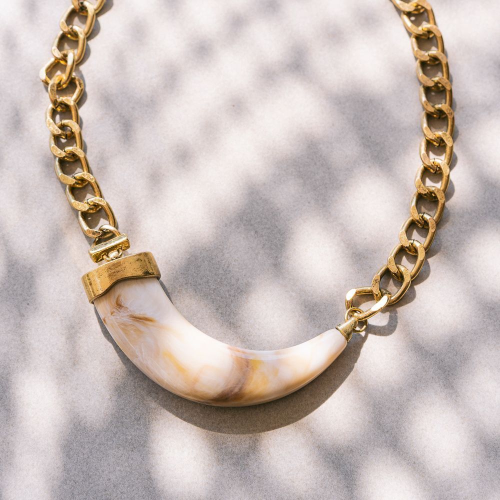 Collar de cadena de oro con un colgante curvo blanco y marrón sobre un fondo estampado claro.