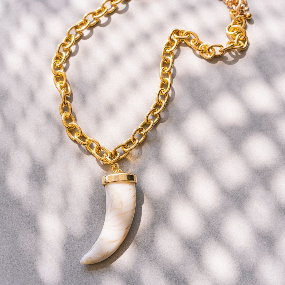 Collar de cadena de oro con un colgante blanco en forma de cuerno sobre un fondo de textura clara.