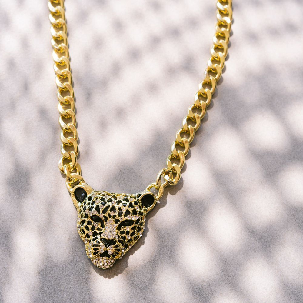 Collar de cadena de oro con un colgante de cabeza de leopardo sobre un fondo estampado.