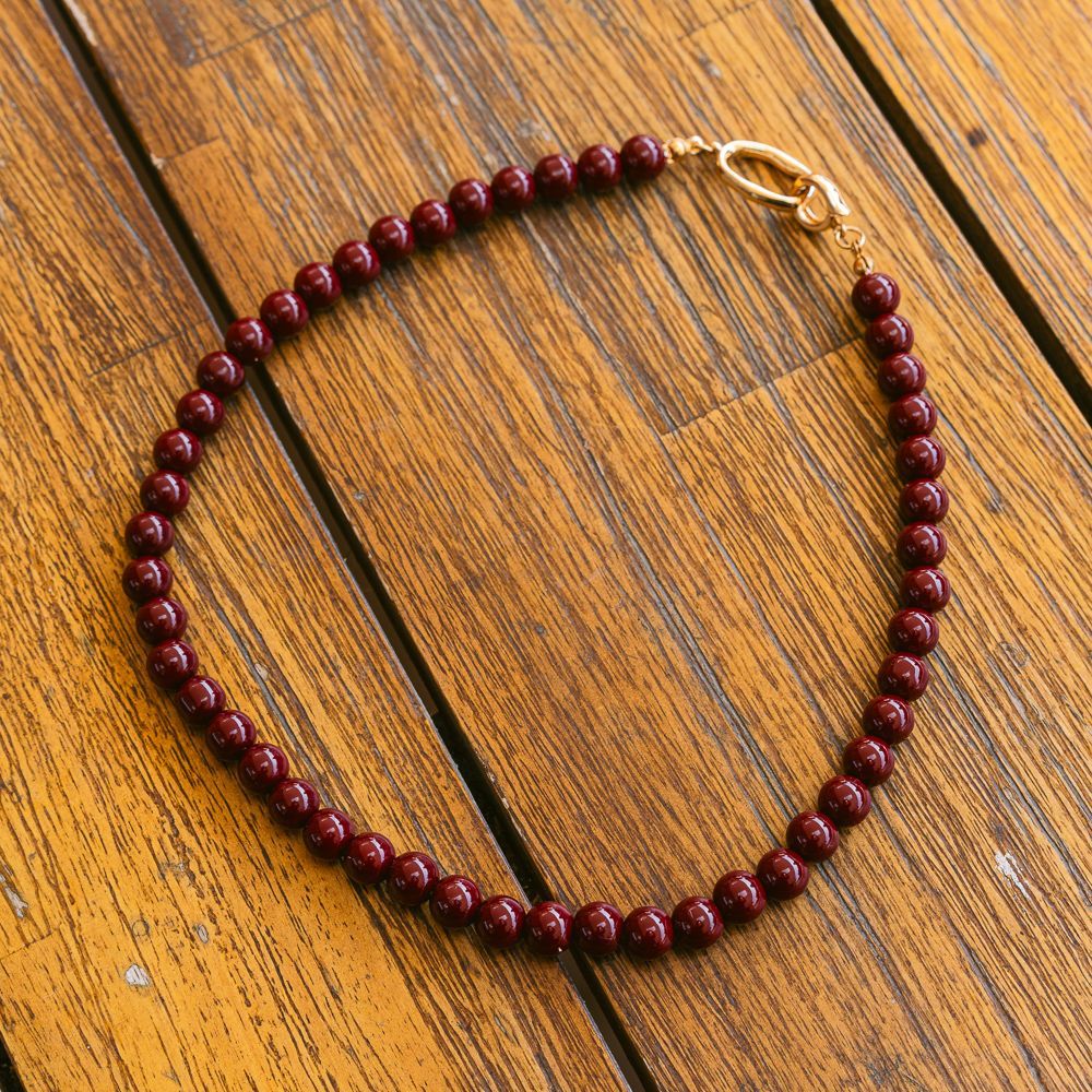 Collar de cuentas color granate con cierre dorado sobre una base de madera.