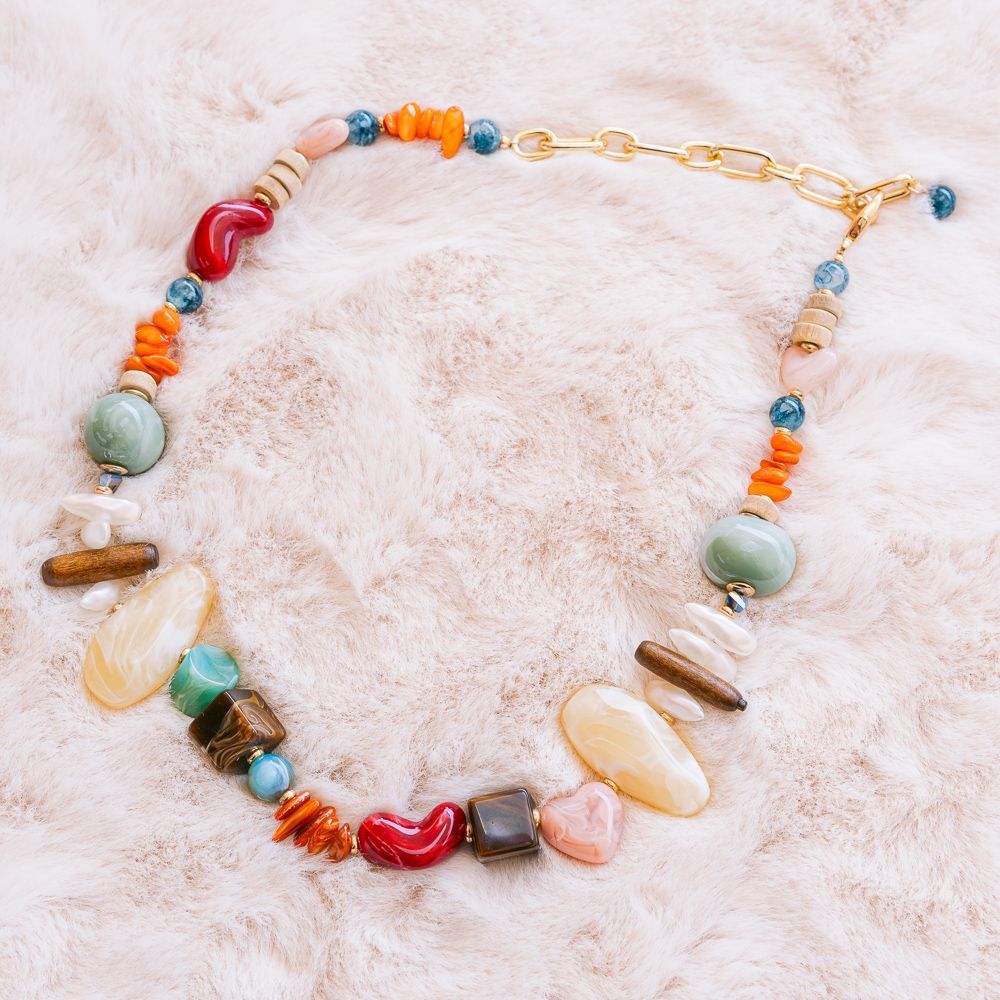 Collar de cuentas coloridas con dijes de conchas y piedras sobre un fondo blanco esponjoso.
