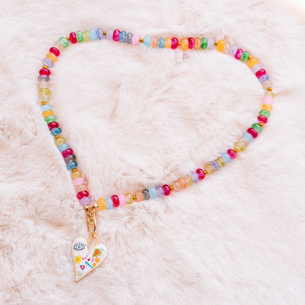 Collar de cuentas de colores con un colgante en forma de corazón sobre un fondo de suave piel rosa.