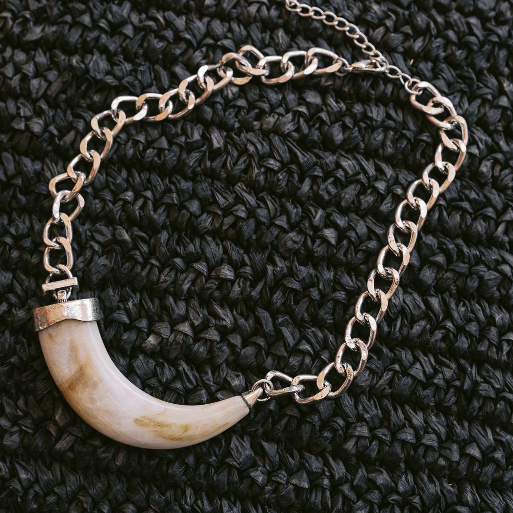 Collar de cadena de oro con colgante de colmillo blanco curvado sobre fondo de punto oscuro.