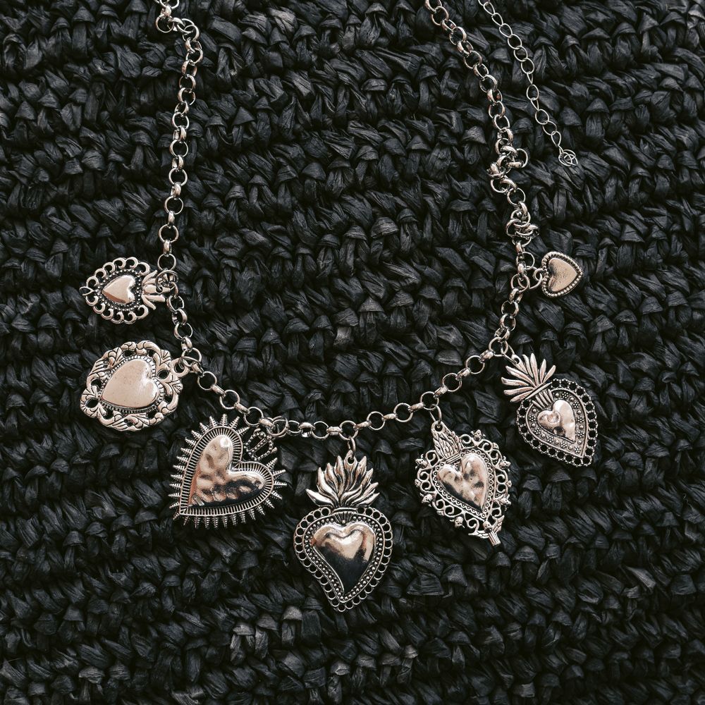 Collar con dije en forma de corazón plateado sobre un fondo de punto oscuro.
