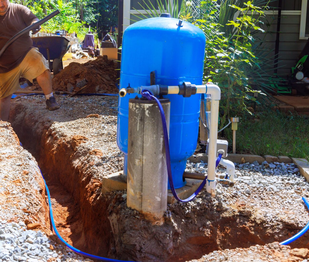 Man working on a well water system with a blue tank in a trench.