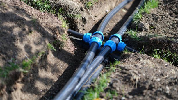 Black pipes with blue connectors in a trench, ready for burial in a garden.