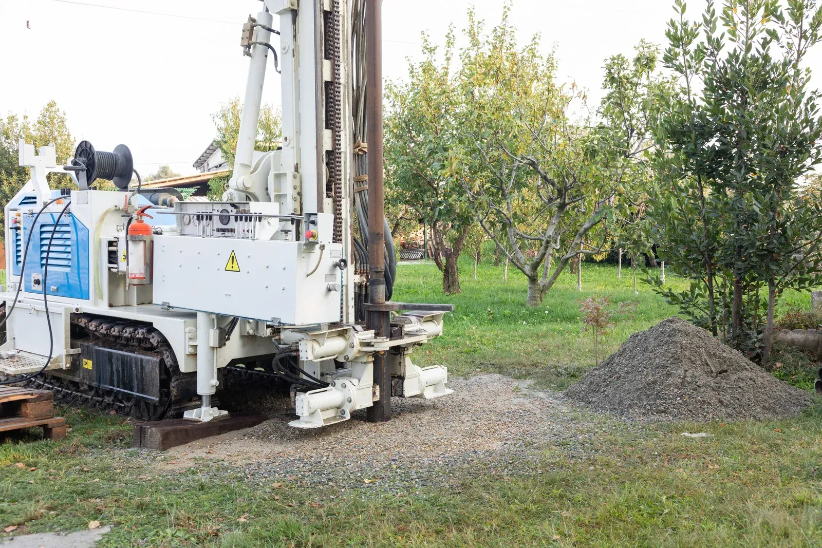 Drilling rig boring into soil, outdoors. Beige and brown machinery in a grassy setting.