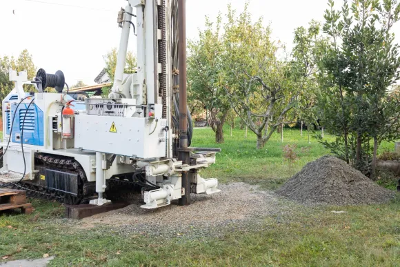Drilling rig boring into soil, outdoors. Beige and brown machinery in a grassy setting.