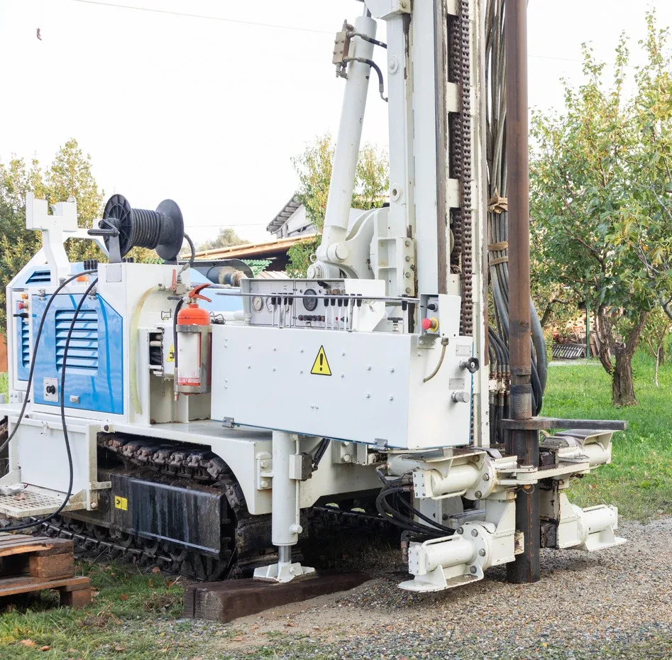 Two people dig around a blue water tank in a yard, removing dirt with shovels.