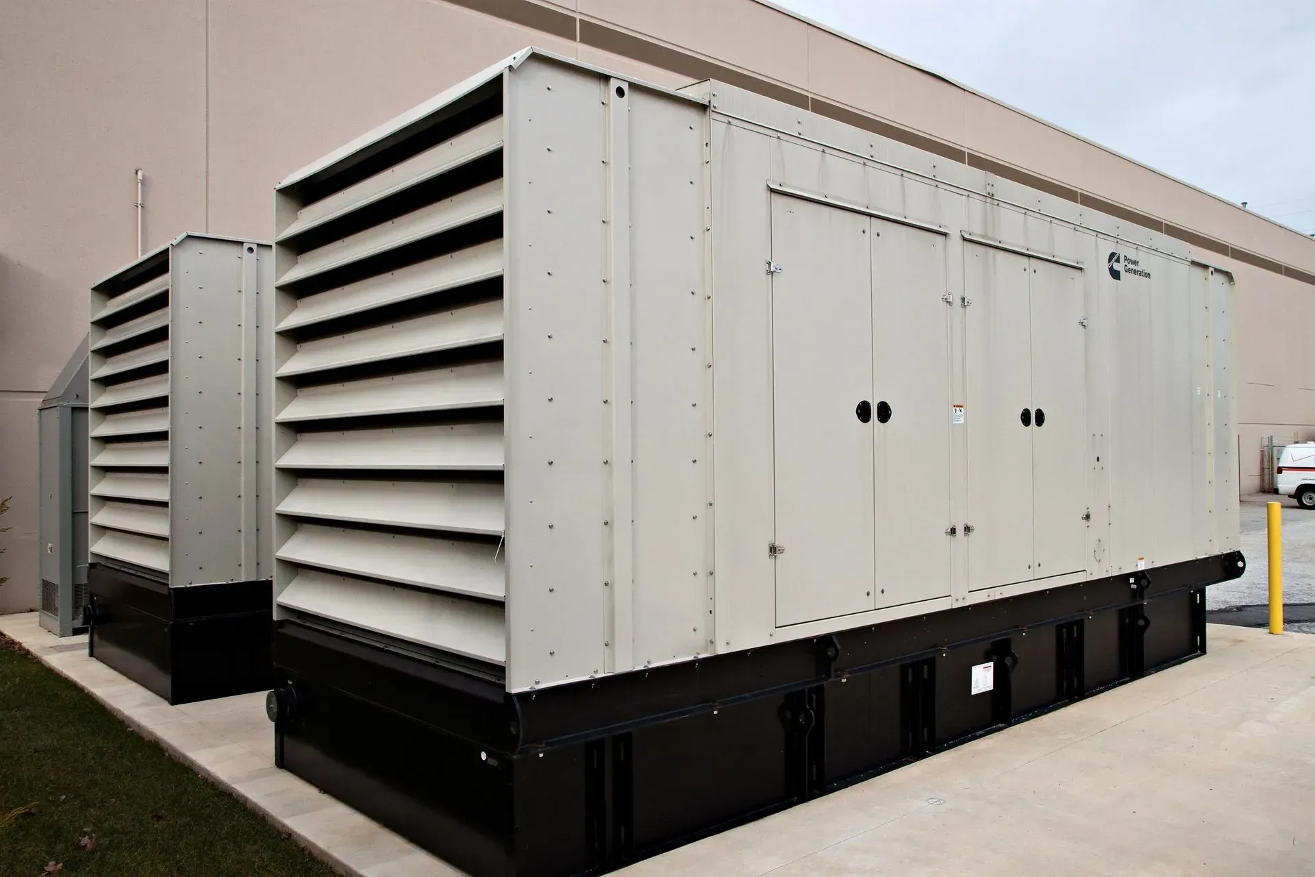 Two large, beige industrial backup generators sit on a concrete pad outside a building.