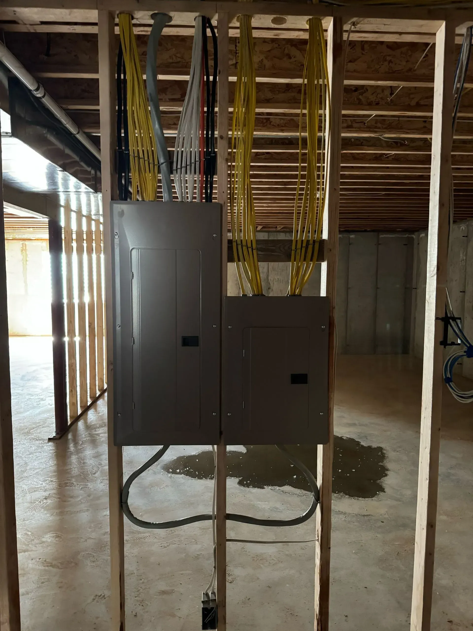 Two electrical breaker panels mounted on wooden wall studs with numerous yellow electrical cables routed from above.