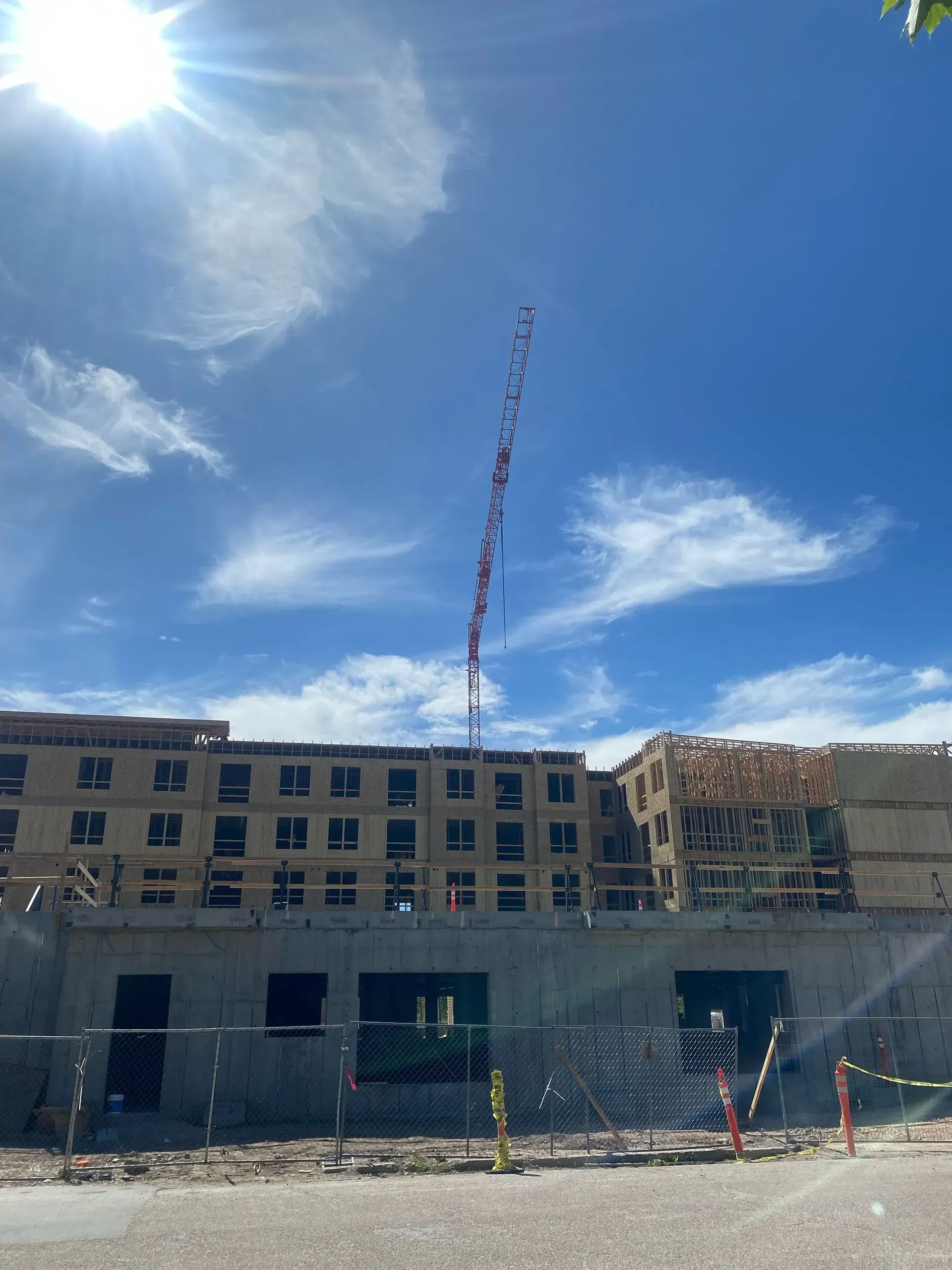 A construction site with a multi-story building frame under a bright blue sky with a visible crane boom.