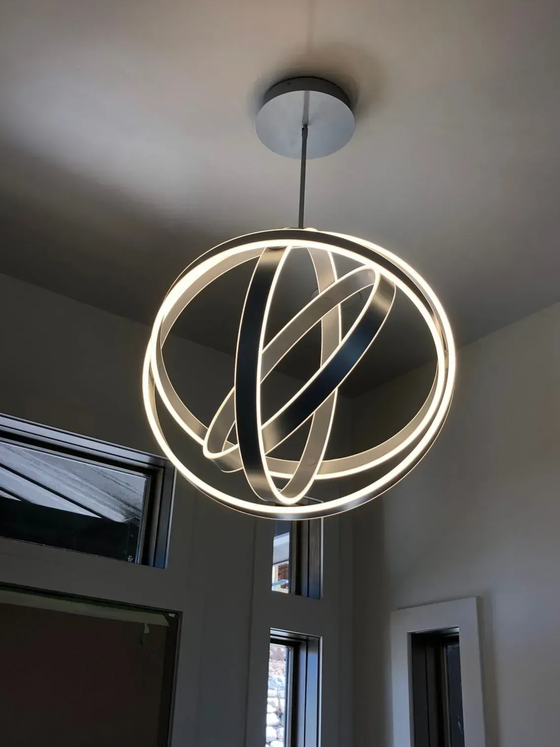 A modern spherical pendant light with three interlocking, glowing LED rings suspended from a silver ceiling mount.