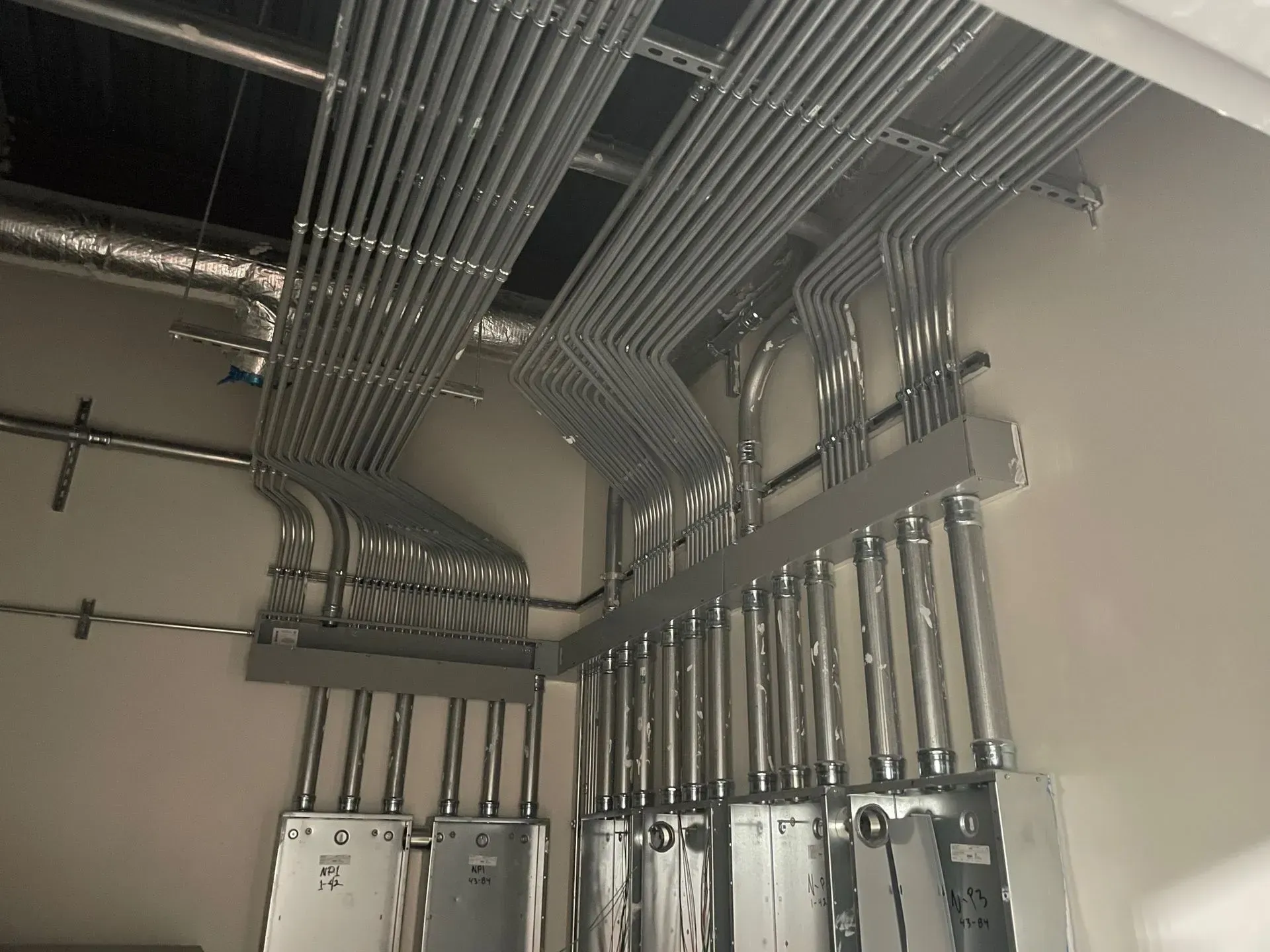 A series of metal electrical conduits run along a wall and ceiling, connecting to junction boxes in an industrial setting.