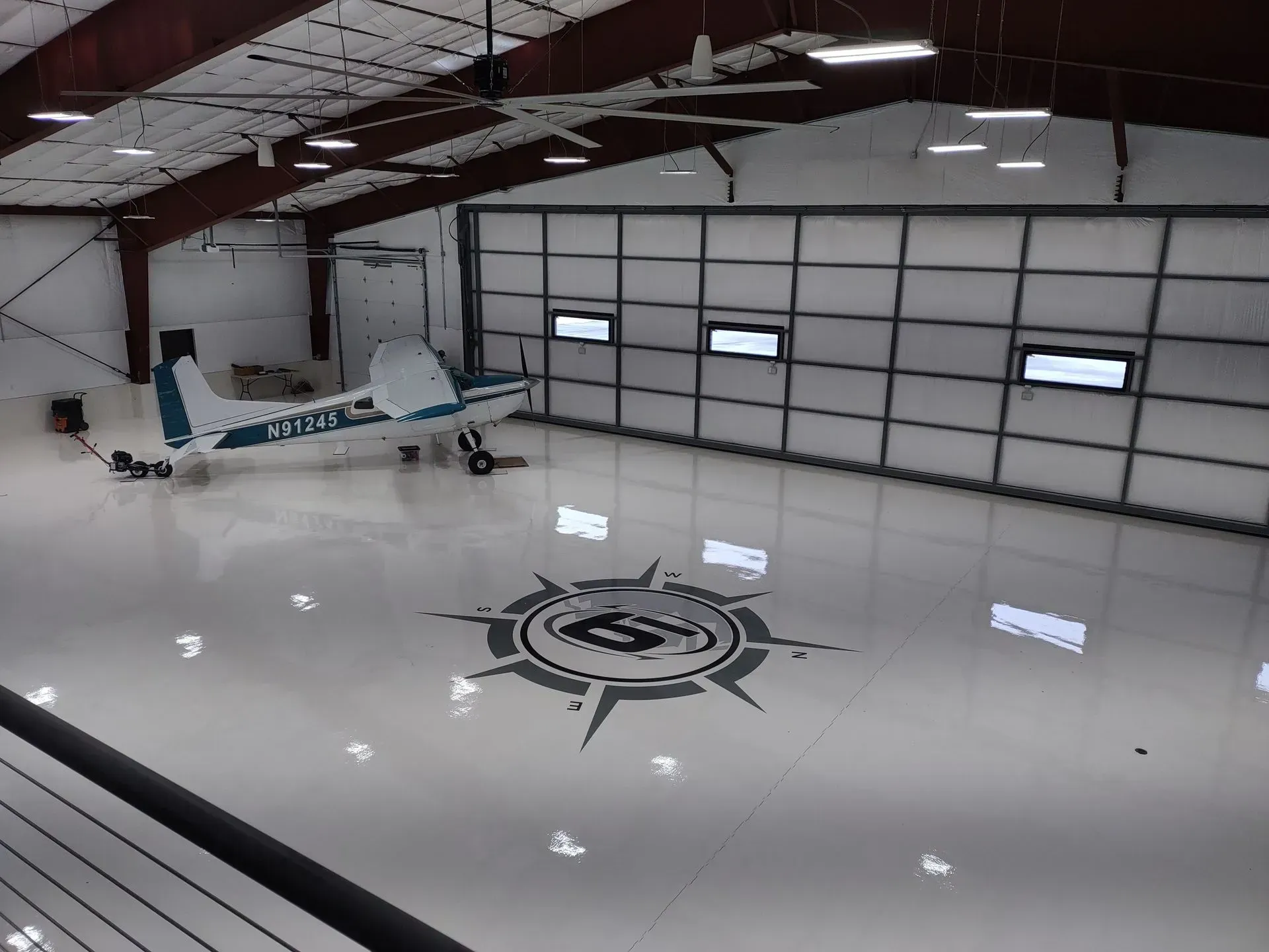 A white light aircraft parked inside a large, clean hangar with a compass rose logo on the polished floor.