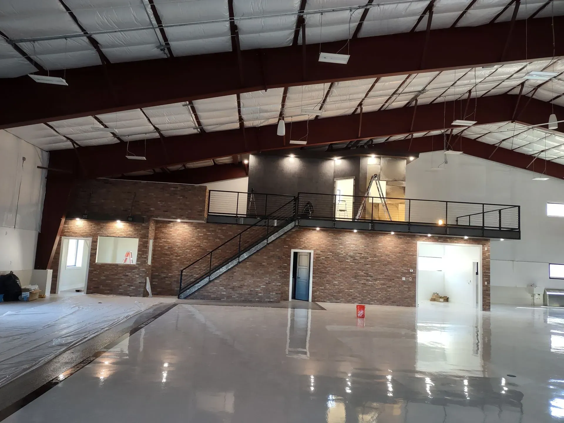 A spacious warehouse interior with a stone-accented mezzanine, staircase, and reflective white floor.
