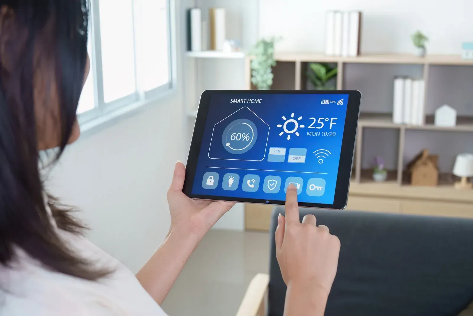 A person uses a tablet displaying a smart home control interface in a bright, modern living room.