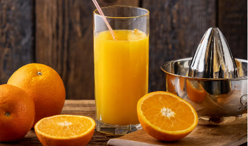 A glass of orange juice with a straw next to oranges and an orange juicer.