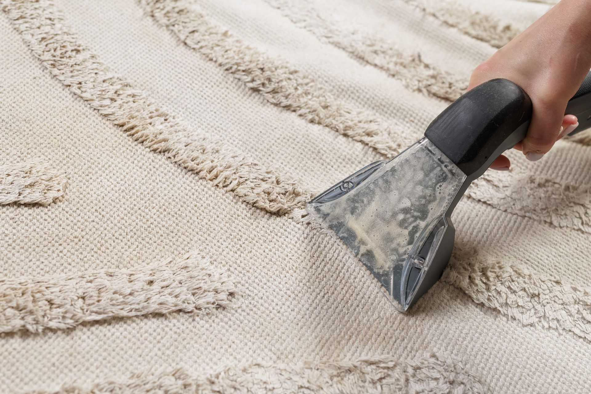 Hand using a carpet cleaner nozzle on a beige rug, removing dirt in parallel lines