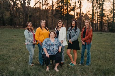 Group of six women posing for a photo outdoors in a field. They are smiling and wearing casual attire.