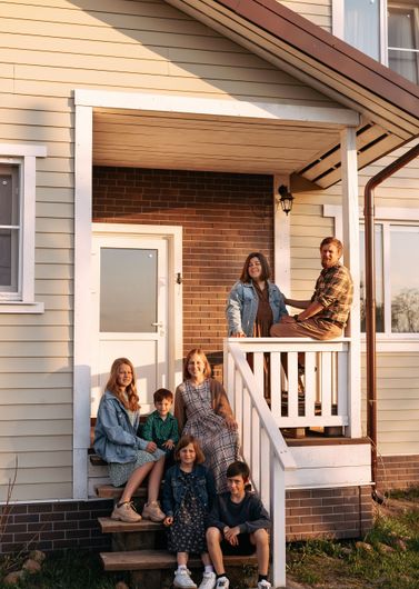 Family poses on the porch of a light-colored house.
