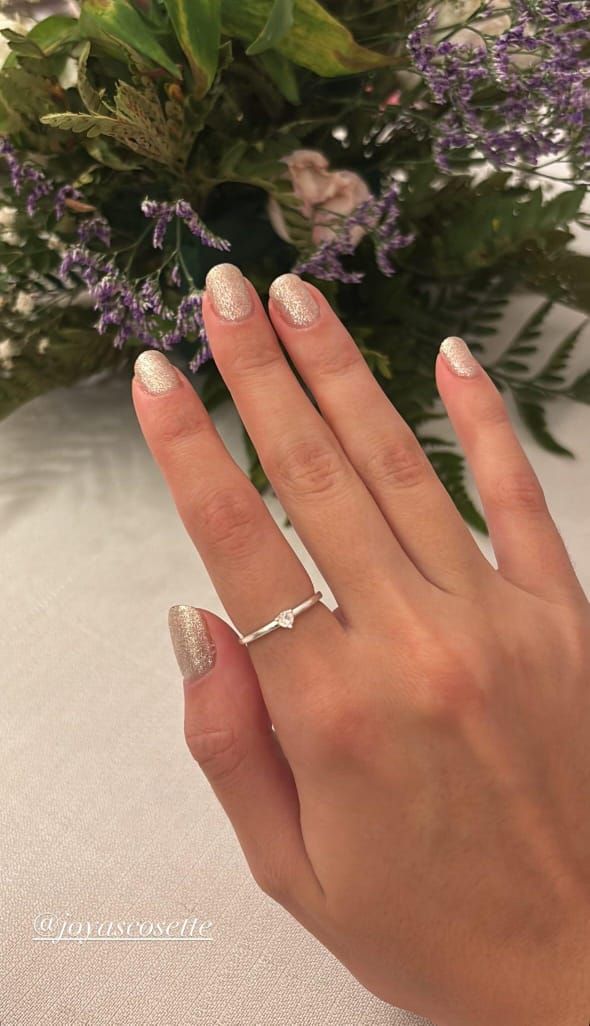 Mano que lleva un anillo de plata con un pequeño diamante, sobre un fondo de flores.