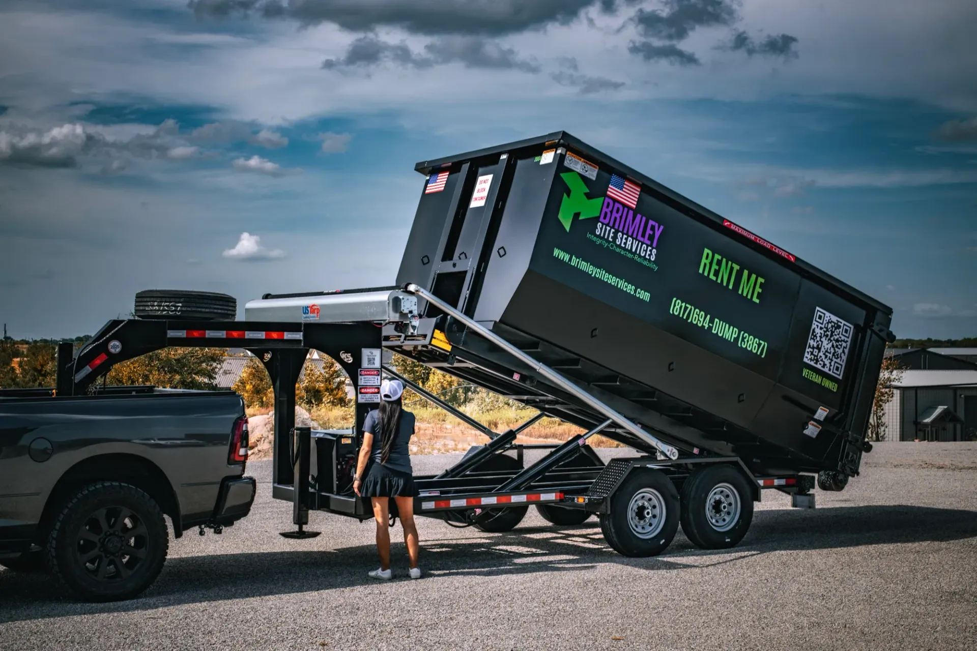 A dumpster is being pulled by a truck on a trailer.