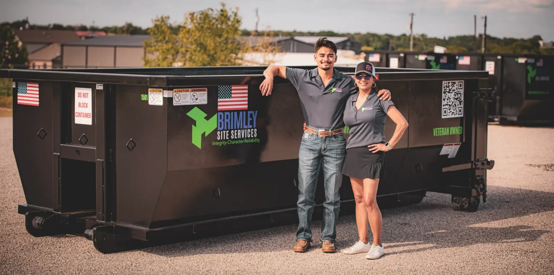A man and a woman are standing in front of a dumpster.