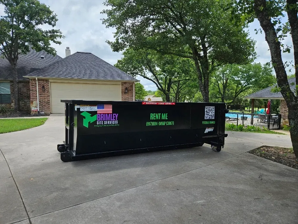A dumpster is parked in a driveway in front of a house.
