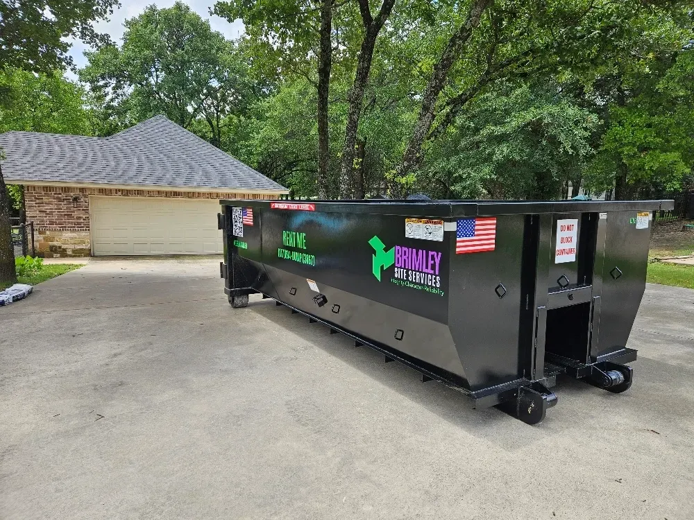 A dumpster is parked in a driveway in front of a house.