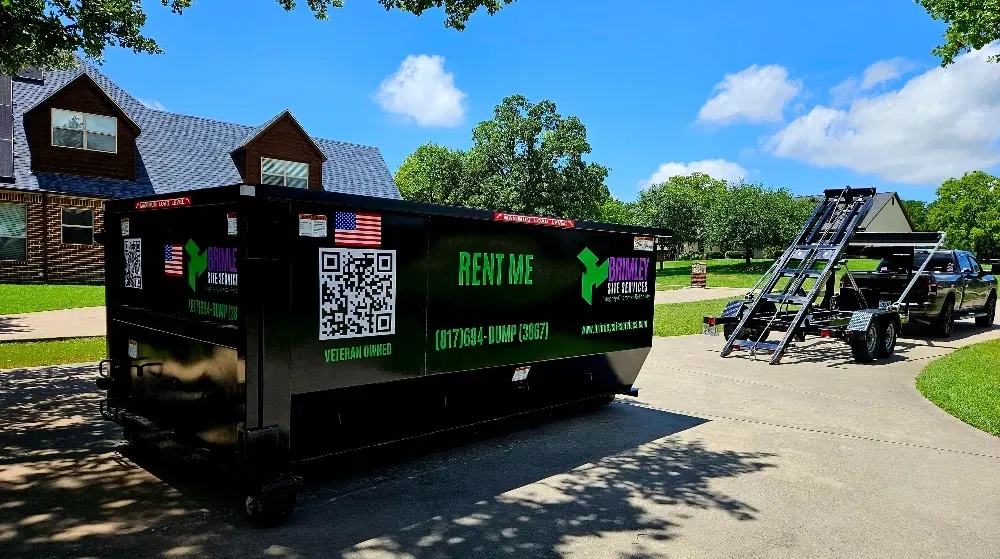 A dumpster is parked in a driveway next to a house.