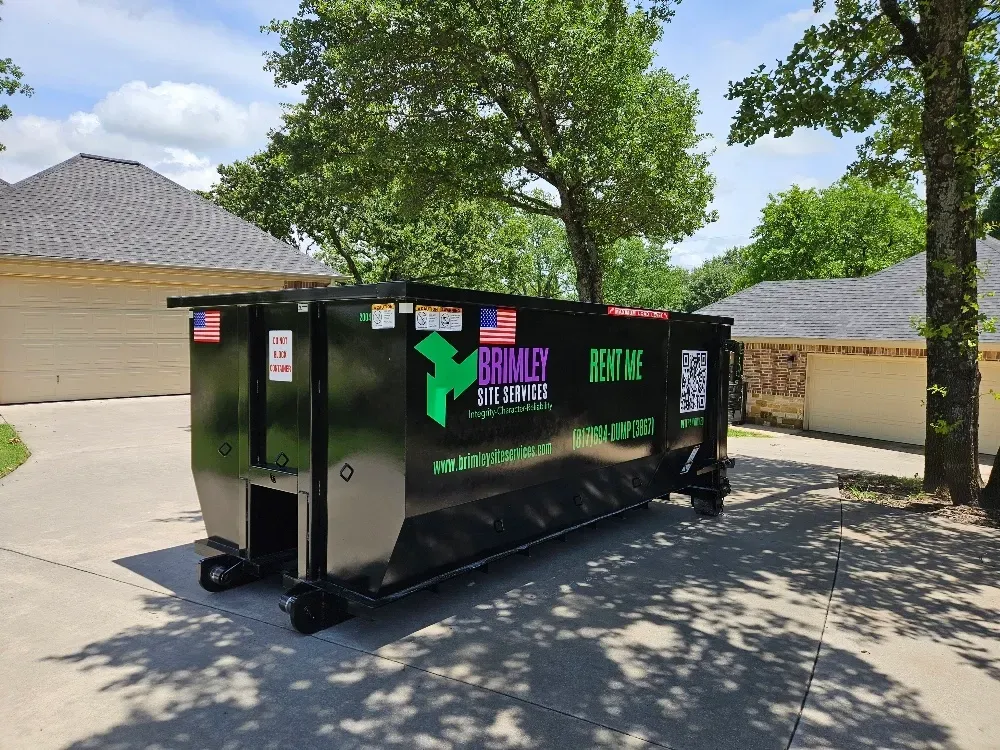 A dumpster is parked in a driveway next to a house.