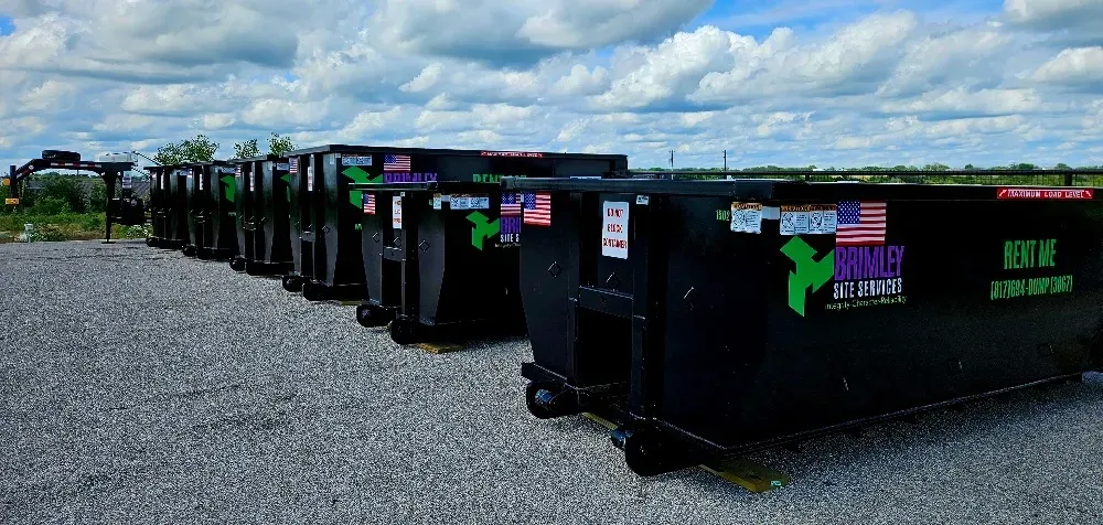 A row of dumpsters are parked in a gravel lot.