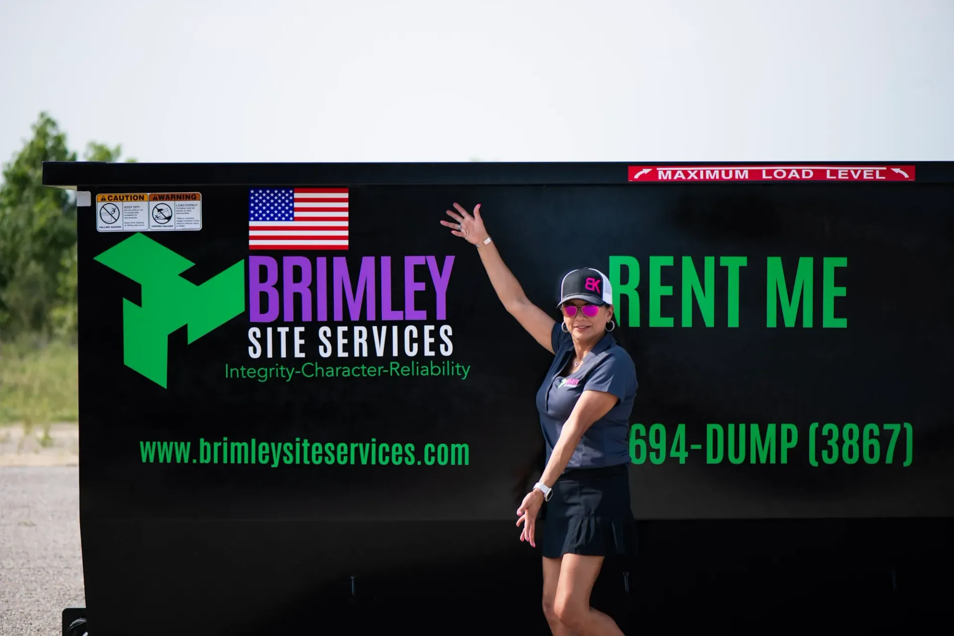 A woman is standing in front of a dumpster that says brimley site services.
