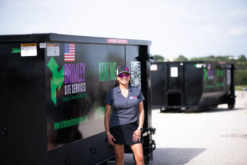 A woman is standing in front of a dumpster.