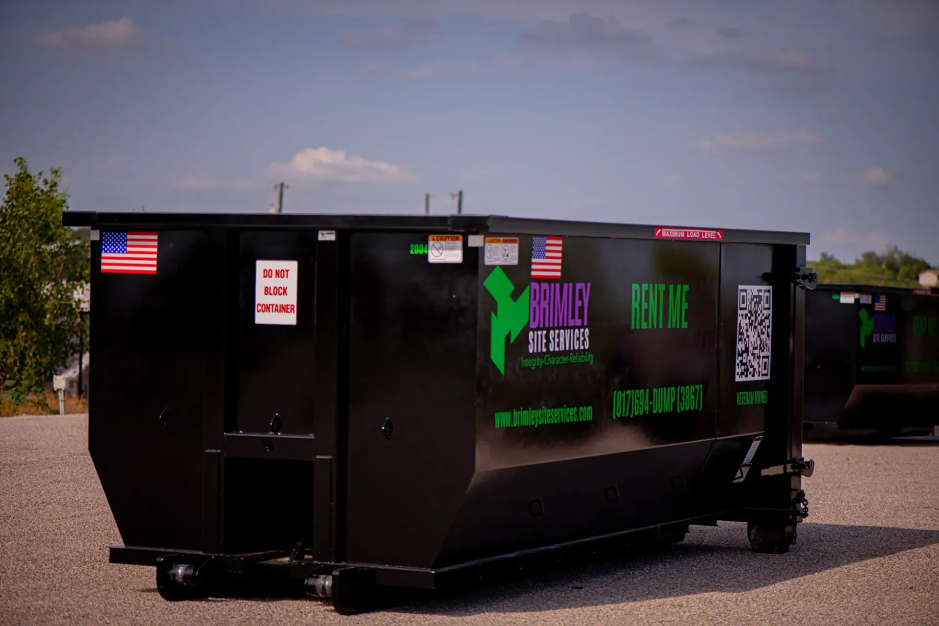 A large black dumpster is parked in a gravel lot.