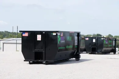 A row of dumpsters are parked in a gravel lot.