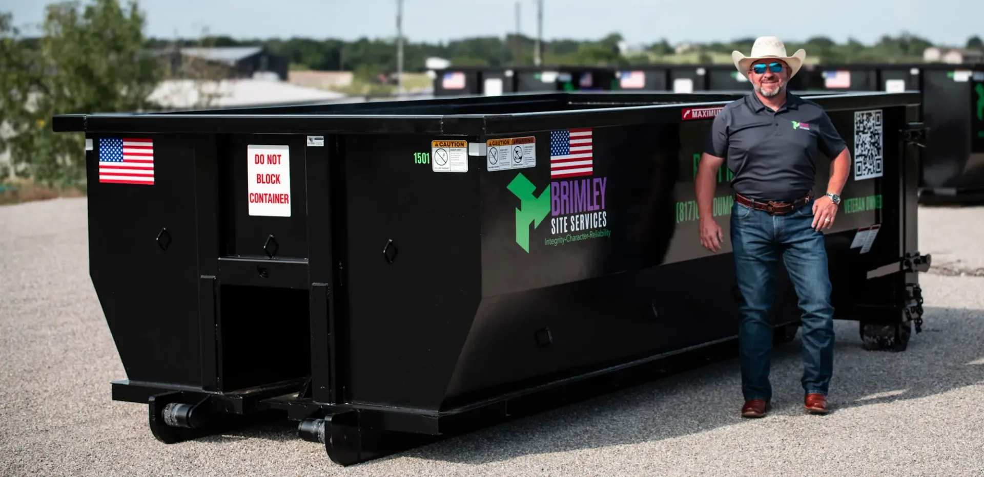 A man in a cowboy hat is standing next to a large dumpster.