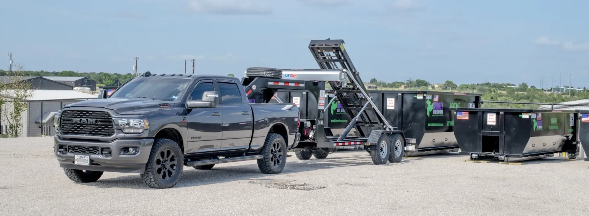 A black truck is towing a dumpster on a trailer.