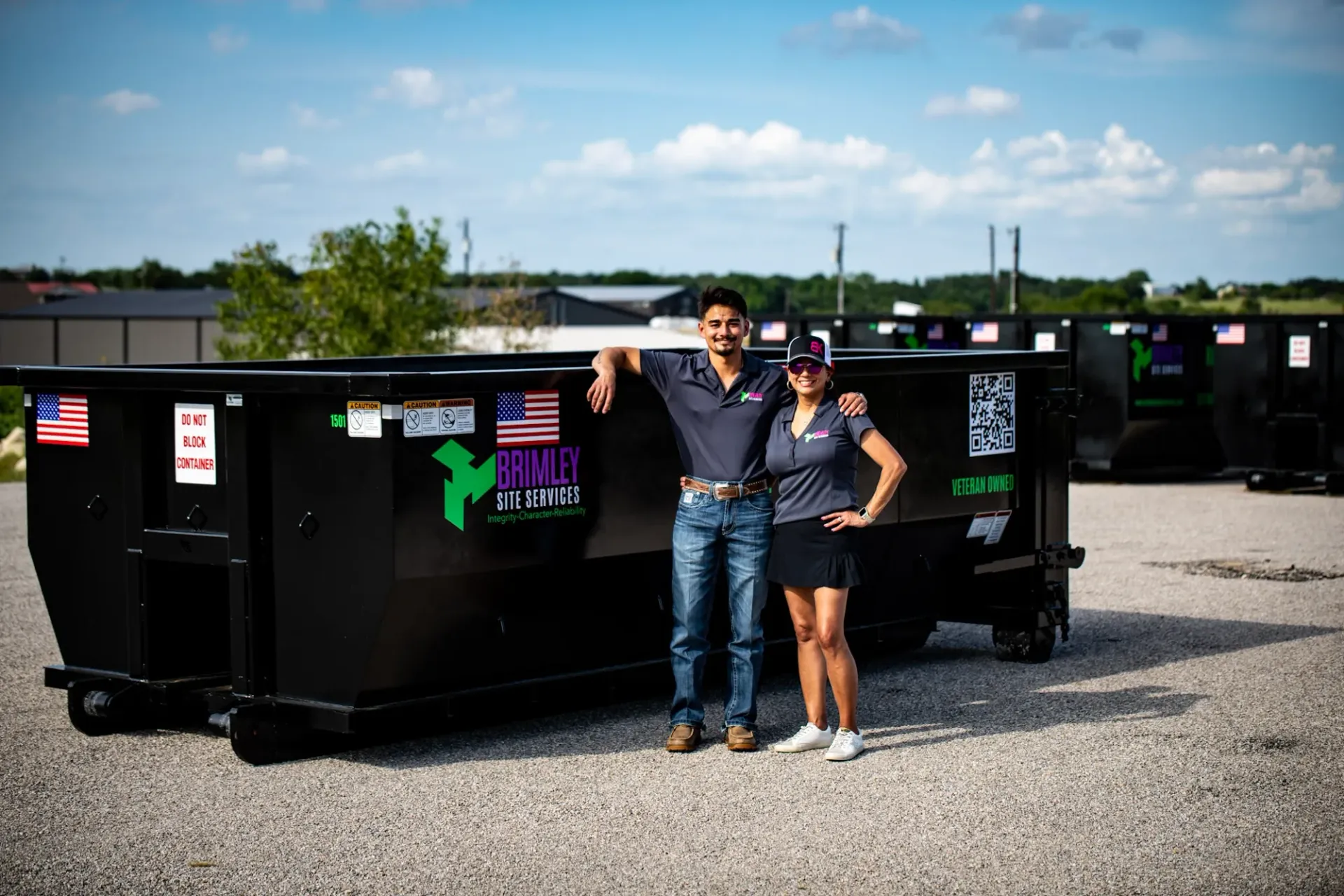 A man and a woman are standing in front of a dumpster.