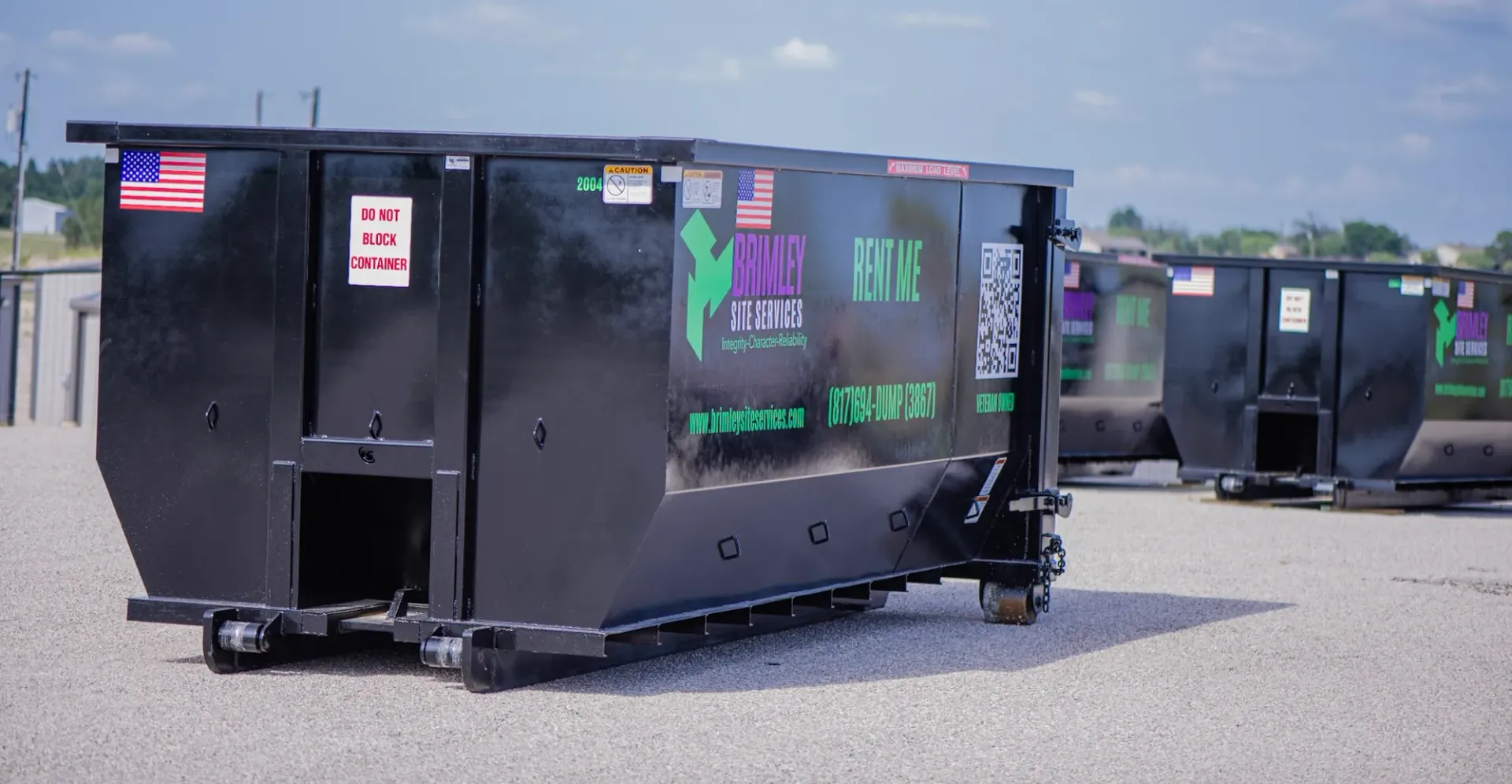 A row of dumpsters are parked in a gravel lot.