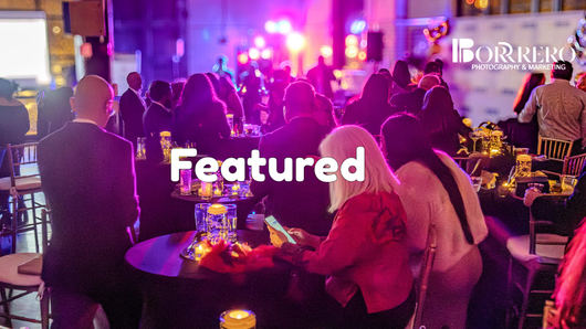 People gather at tables in a dimly lit, purple-hued event space.