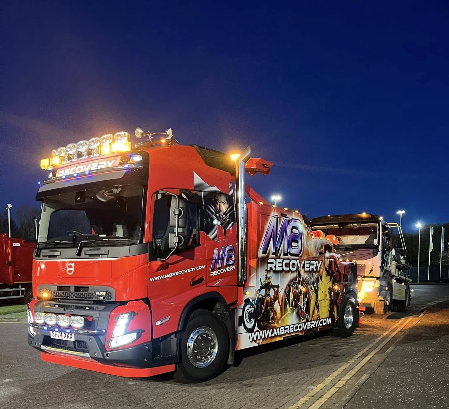 Red tow truck with lights towing another truck at night. 