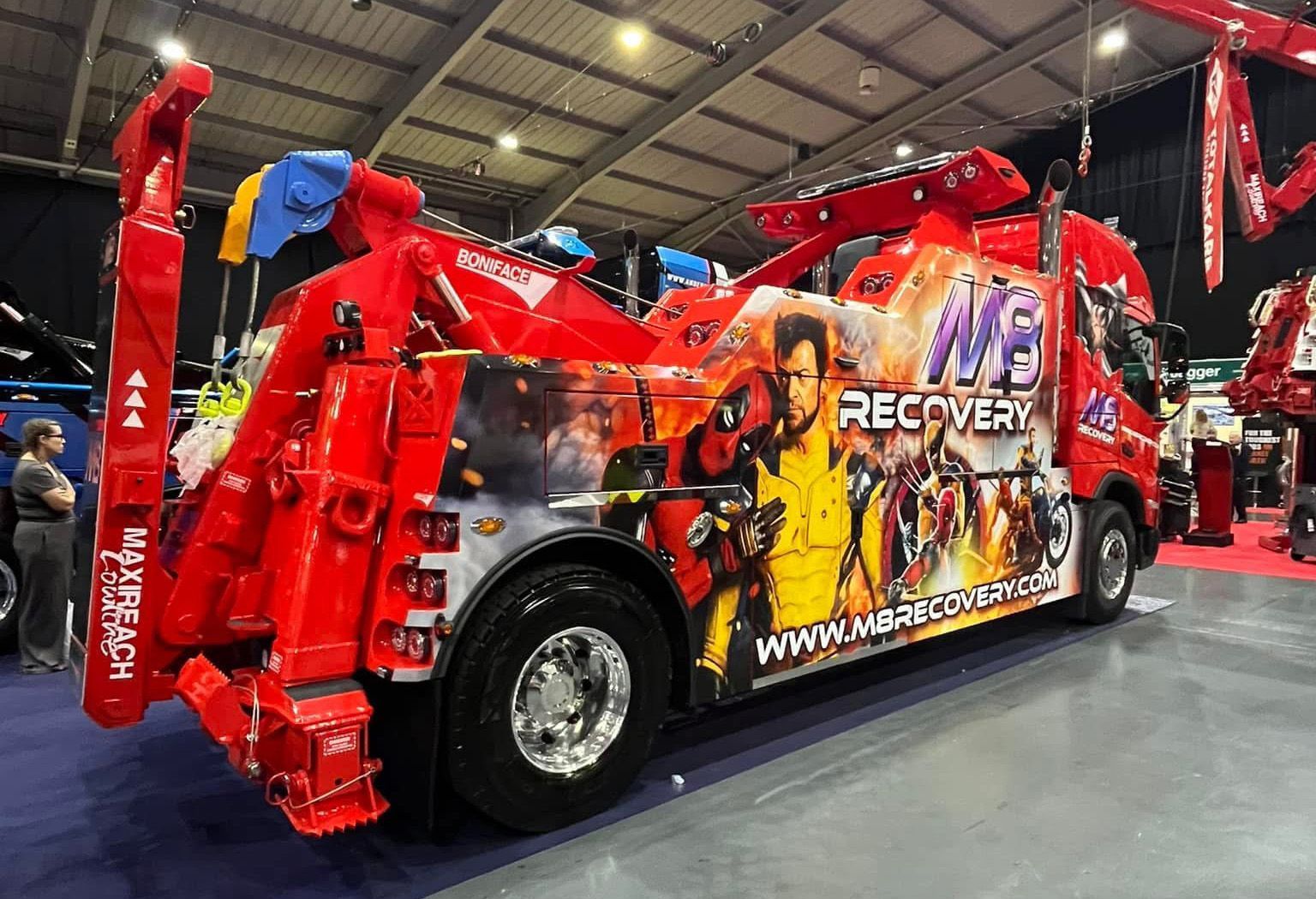 Red tow truck with superhero-themed graphics at a show.