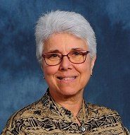 A woman wearing glasses and a patterned shirt is smiling for the camera.